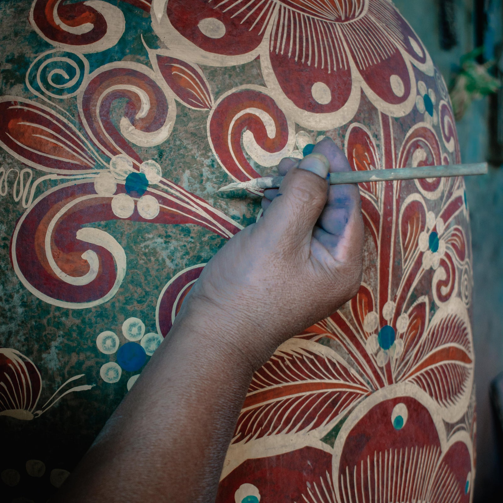 hand with brush paints ornate vase