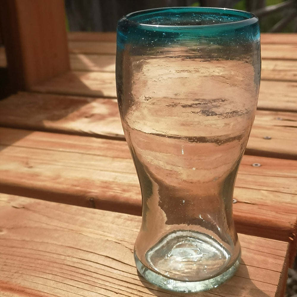 Tall cola glass with aqua colored rim on a deck