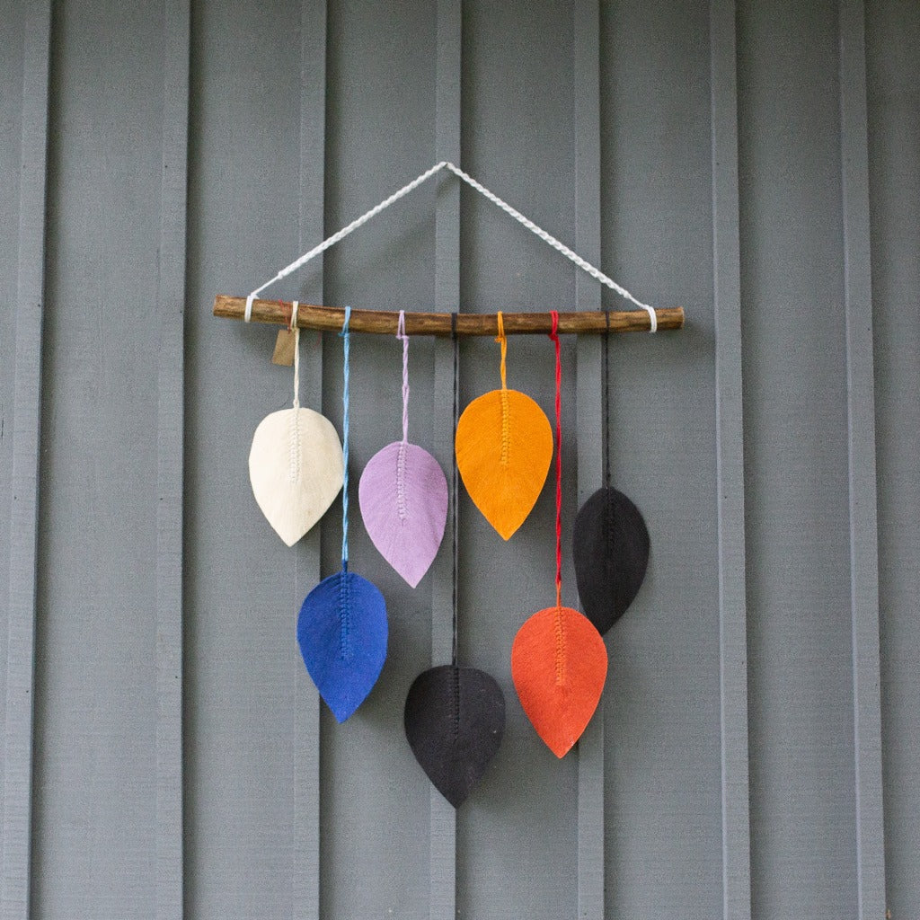 Hanging macrame wall decor featuring colourful leaves hanging from branch on a blue barn board background