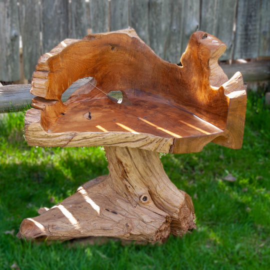 A natural teak wood chair, heavy looking, like it was carved from a tree stump