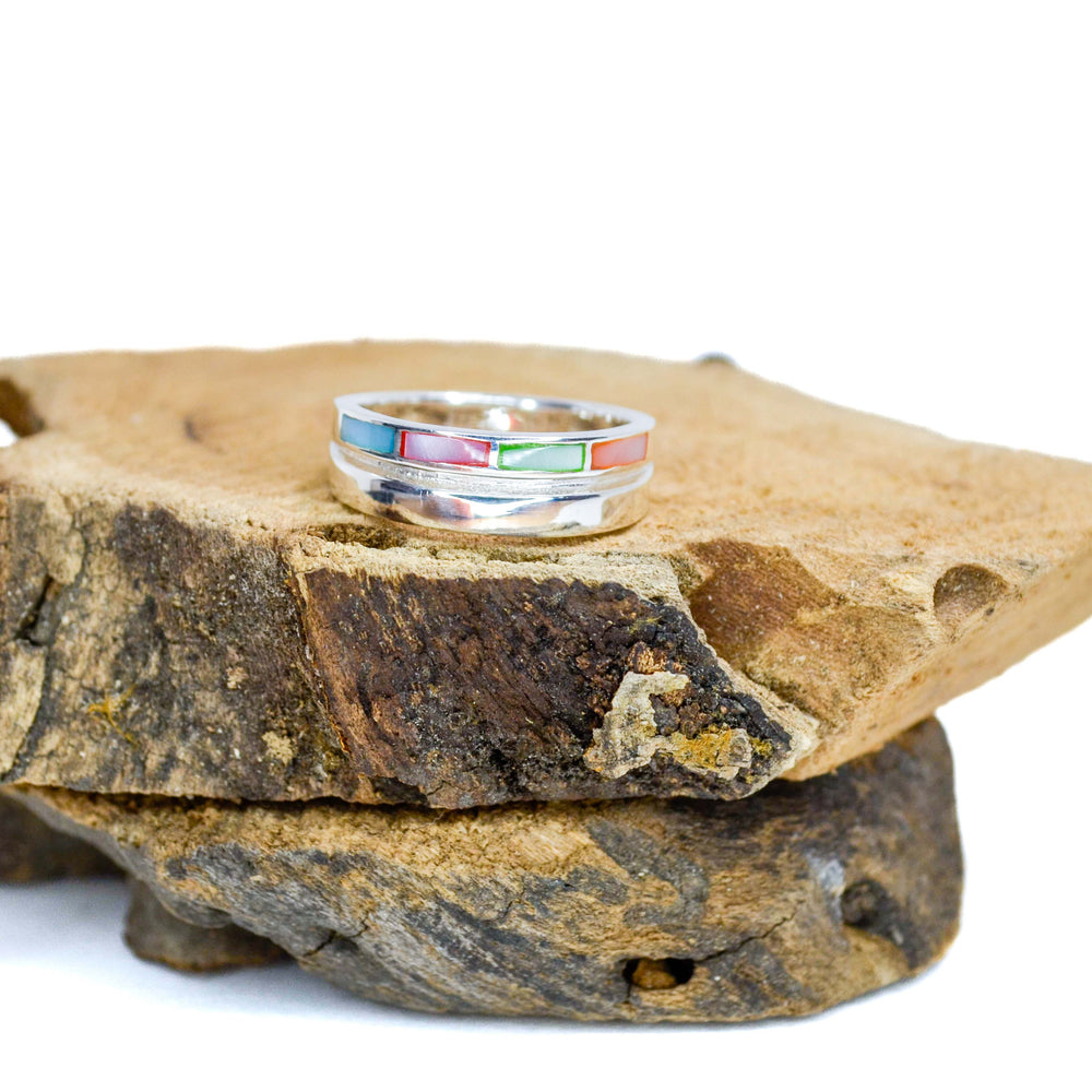 stacked design with rainbow inlaid pieces silver ring sitting on piece of wood