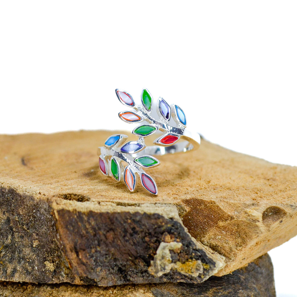 Floral design with rainbow inlaid pieces silver ring sitting on piece of wood
