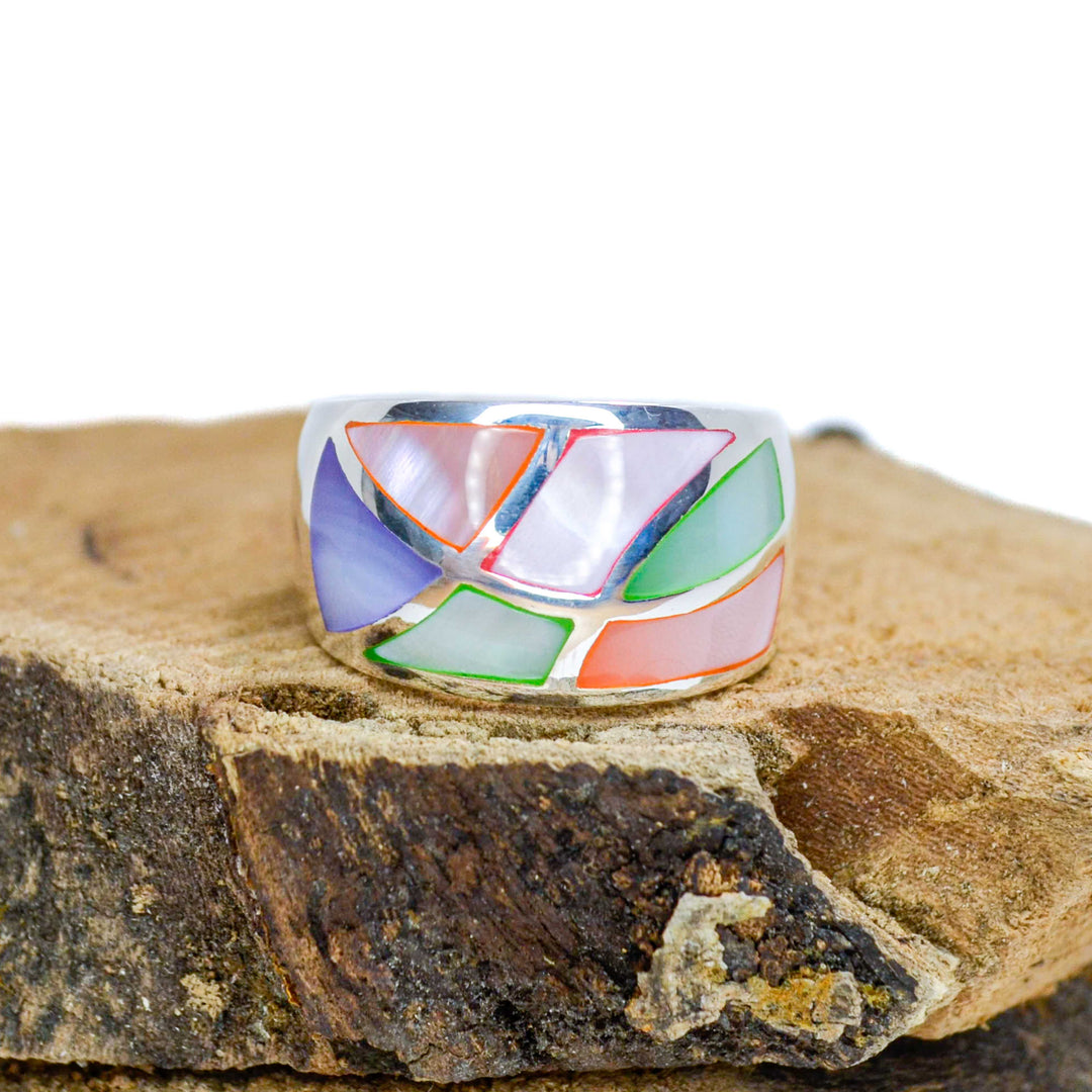 Abstract design with rainbow inlaid pieces silver ring sitting on piece of wood